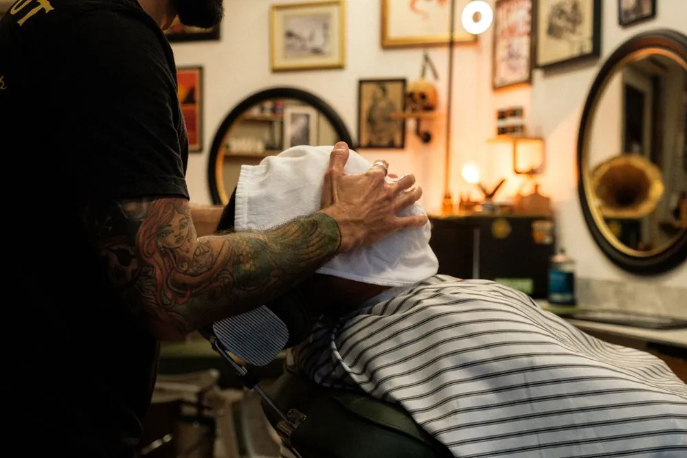 Serviette chaude posée sur le visage d'un client, miroirs ronds et lumière tamisée en fond